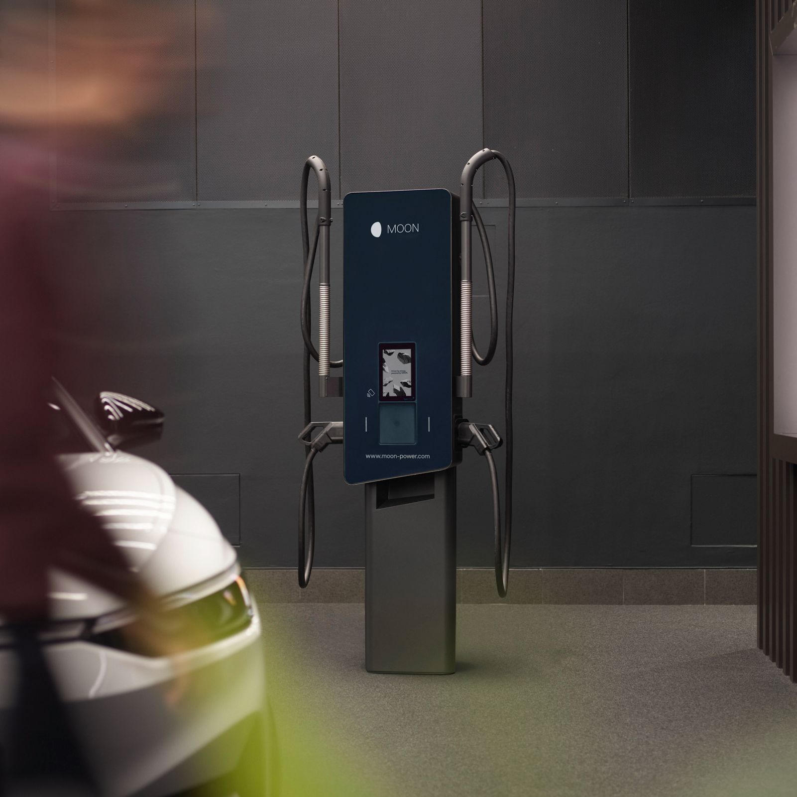 Wallbox vor einer grauen Wand mit E-Auto im Vordergrund