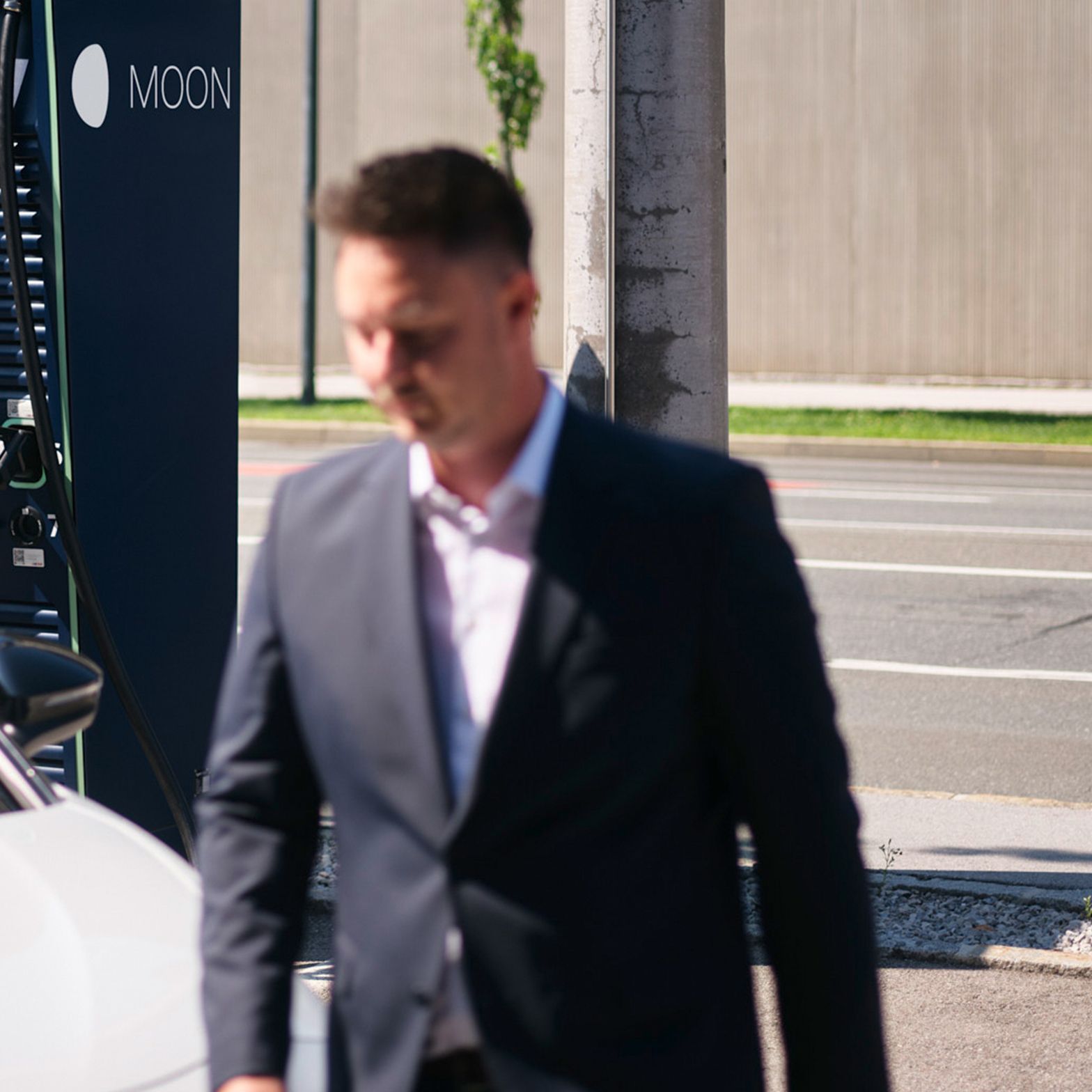 Muškarac hoda ispred automobila ispred stanice za punjenje