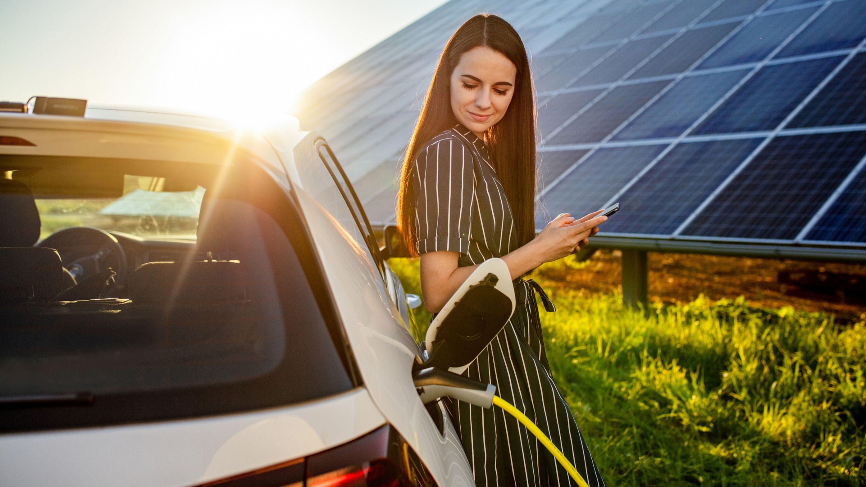 Žena naslonjena na puneći automobil ispred fotonaponskog sustava
