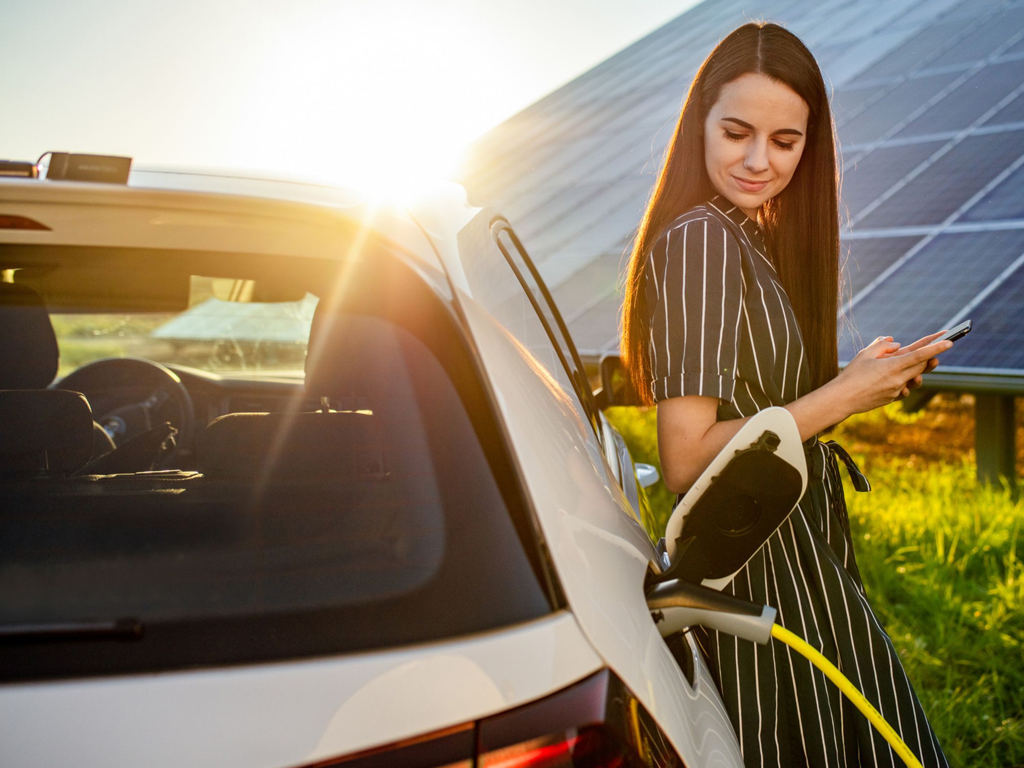Žena naslonjena na puneći automobil ispred fotonaponskog sustava