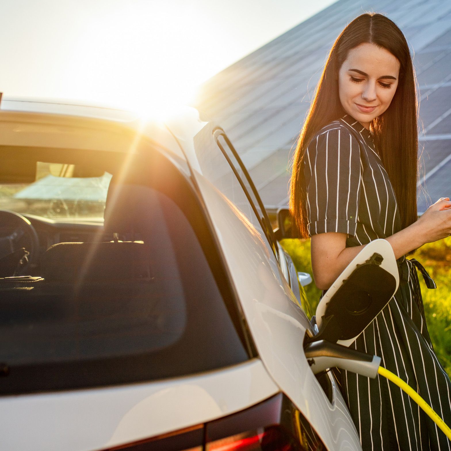 Žena naslonjena na puneći automobil ispred fotonaponskog sustava