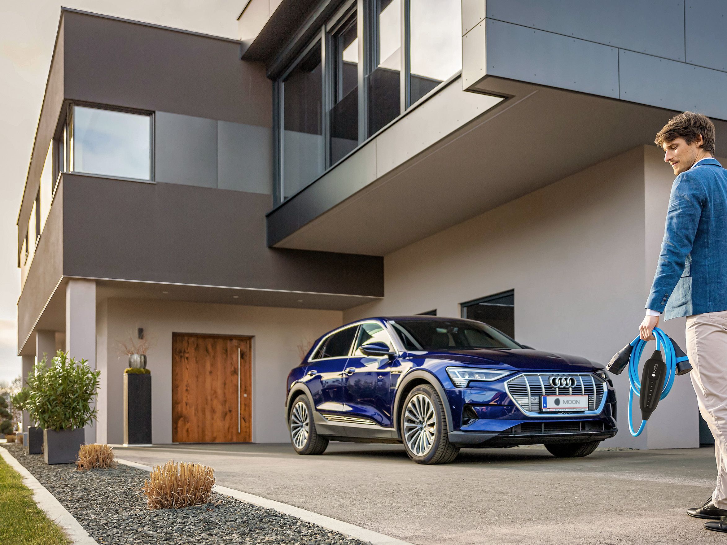 Muškarac hoda prema automobilu blizu kuće s kabelom u ruci